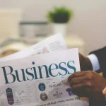 Businessman reading a financial newspaper with business charts and stock prices.