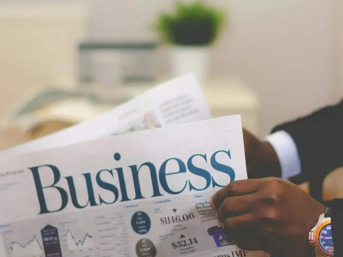 Businessman reading a financial newspaper with business charts and stock prices.