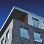 Modern building corner with a mix of brick and metal facade under a deep blue sky.