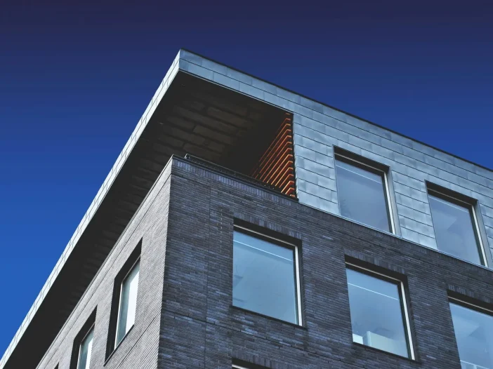Modern building corner with a mix of brick and metal facade under a deep blue sky.